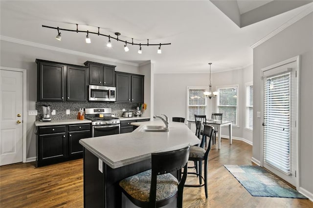 kitchen featuring decorative light fixtures, an island with sink, a kitchen bar, appliances with stainless steel finishes, and sink