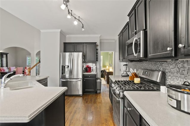 kitchen with stainless steel appliances, sink, backsplash, a center island with sink, and crown molding