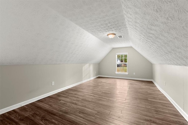 additional living space with a textured ceiling, lofted ceiling, and dark hardwood / wood-style floors