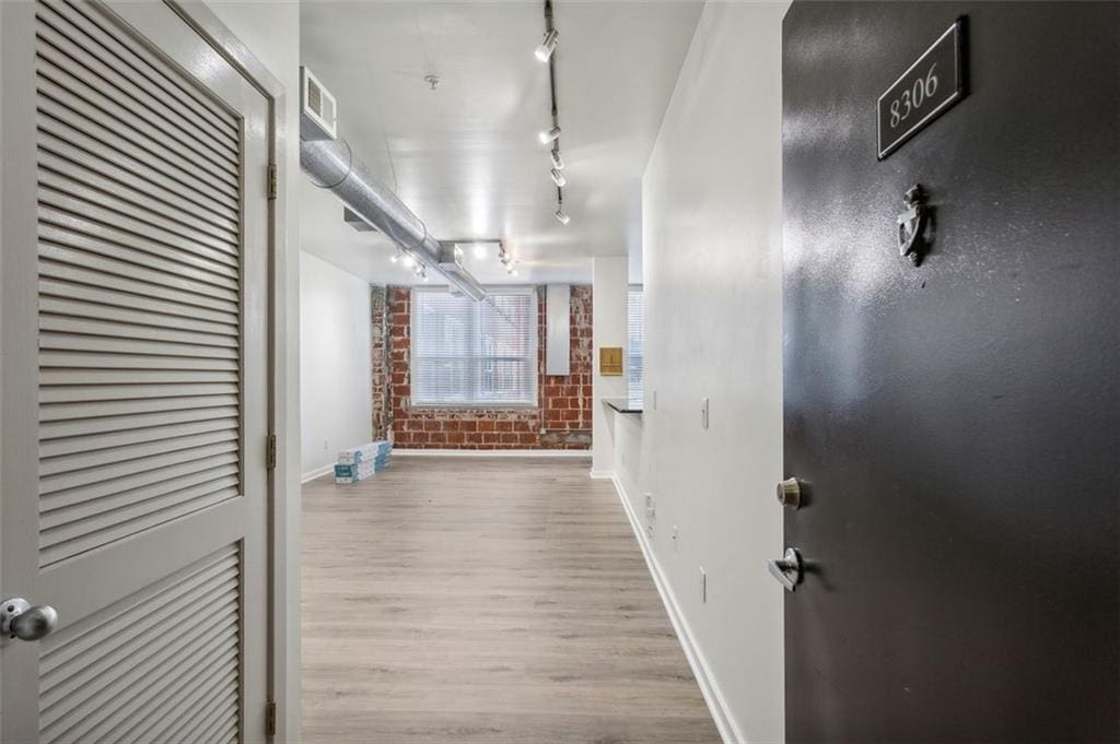 corridor with light wood-type flooring and brick wall