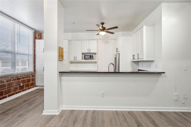 kitchen with brick wall, white cabinets, appliances with stainless steel finishes, kitchen peninsula, and light wood-type flooring