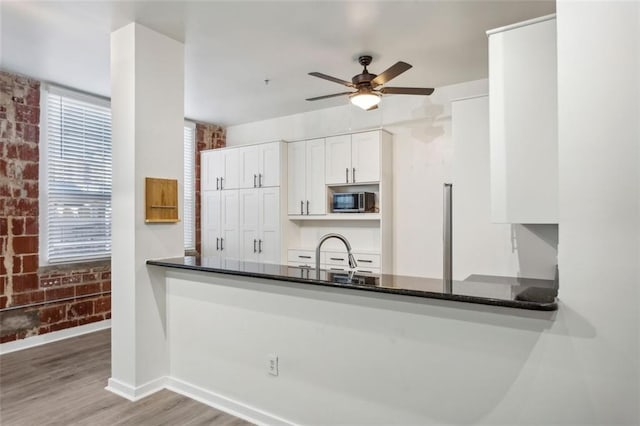 kitchen with brick wall, white cabinets, dark stone countertops, light hardwood / wood-style floors, and kitchen peninsula