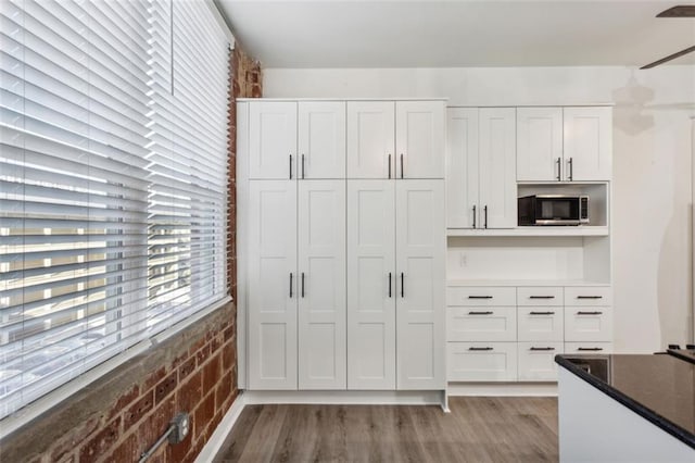 interior space with brick wall, light hardwood / wood-style flooring, white cabinets, and dark stone counters