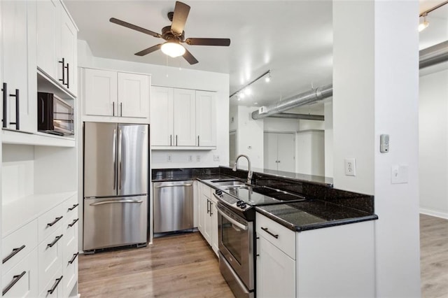 kitchen with dark stone countertops, sink, white cabinetry, light hardwood / wood-style flooring, and appliances with stainless steel finishes