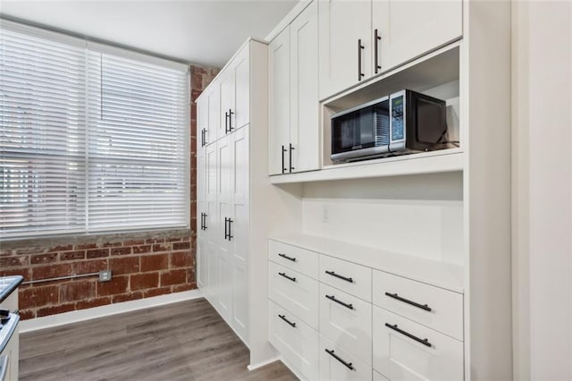 kitchen with brick wall, white cabinets, dark hardwood / wood-style floors, and a wealth of natural light