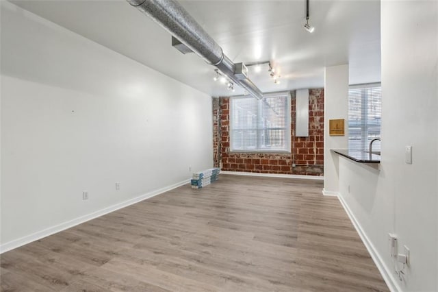 unfurnished living room featuring a healthy amount of sunlight, brick wall, and hardwood / wood-style floors