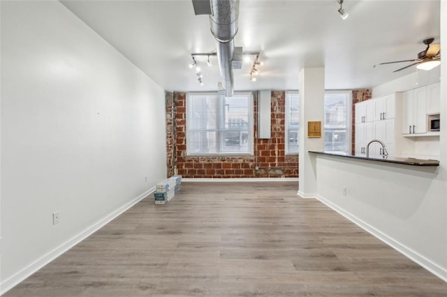 interior space featuring light wood-type flooring, ceiling fan, and brick wall