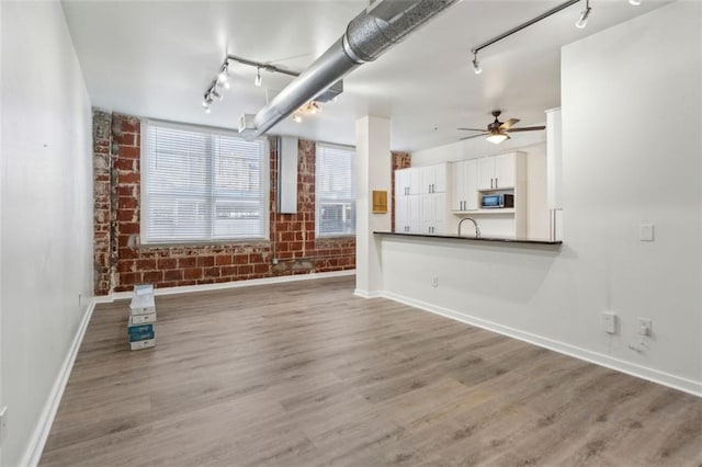 unfurnished living room with ceiling fan, sink, brick wall, and hardwood / wood-style floors