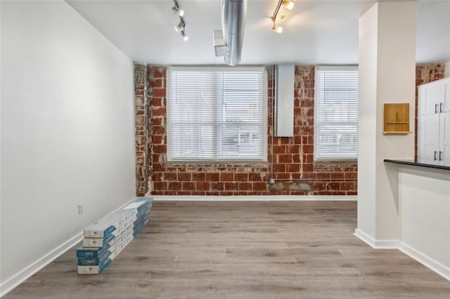 spare room featuring brick wall, hardwood / wood-style flooring, and rail lighting