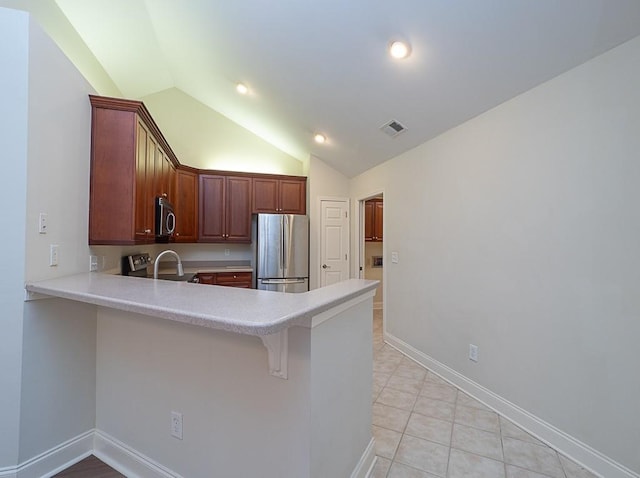 kitchen featuring kitchen peninsula, appliances with stainless steel finishes, vaulted ceiling, and a breakfast bar area