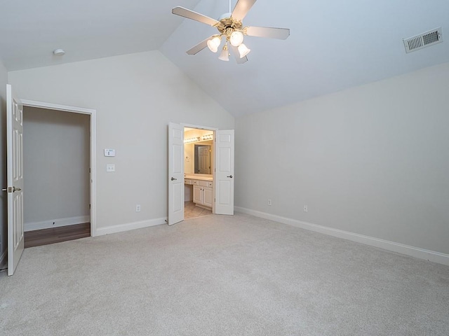 unfurnished bedroom with ceiling fan, ensuite bath, light carpet, and vaulted ceiling