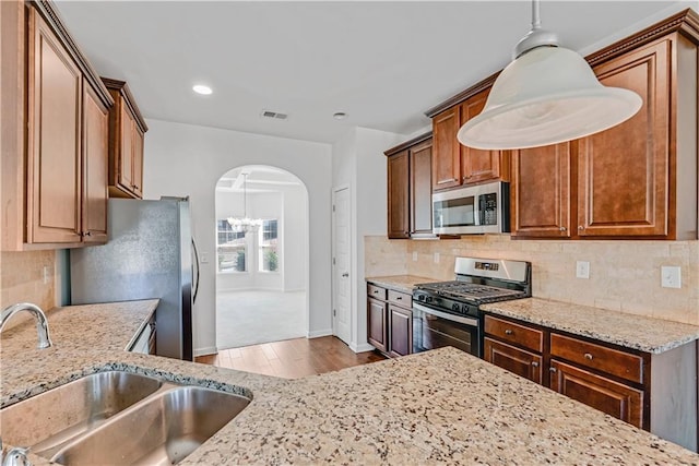 kitchen featuring arched walkways, stainless steel appliances, visible vents, a sink, and light stone countertops