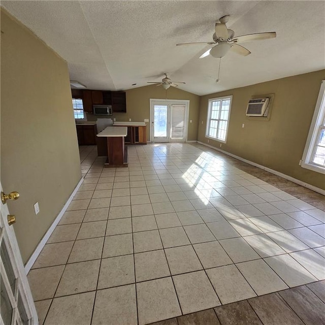 interior space featuring light tile patterned floors, a textured ceiling, lofted ceiling, baseboards, and a wall mounted air conditioner