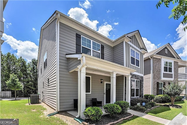 view of front facade with covered porch, central AC unit, board and batten siding, and a front yard