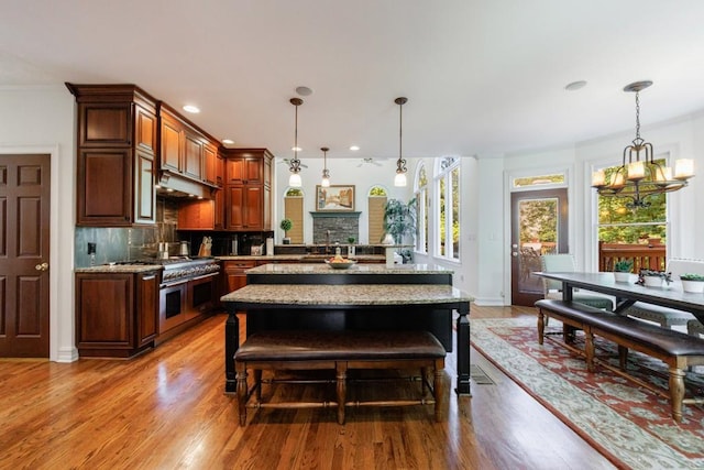 kitchen featuring double oven range, light wood-style floors, backsplash, hanging light fixtures, and recessed lighting
