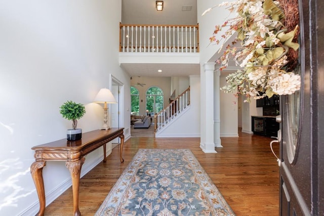 foyer with wood finished floors, a high ceiling, ornate columns, stairway, and baseboards