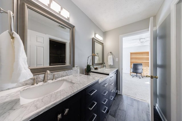 bathroom featuring double vanity, ceiling fan, wood finished floors, and a textured ceiling