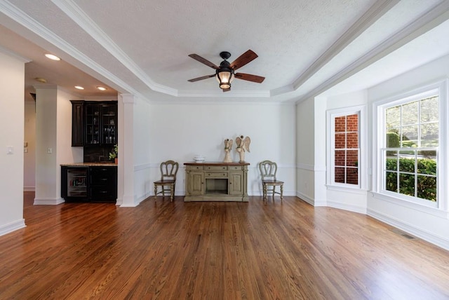 living area with a tray ceiling, wood finished floors, a ceiling fan, crown molding, and baseboards