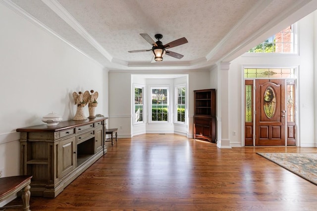 entrance foyer featuring plenty of natural light, wood finished floors, a ceiling fan, a raised ceiling, and ornamental molding