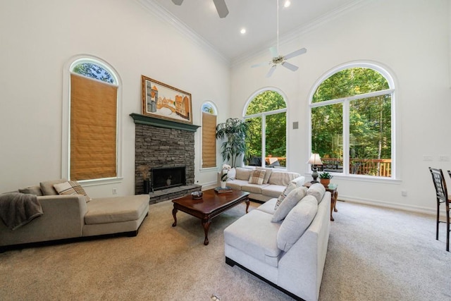 living area featuring ceiling fan, a towering ceiling, carpet, healthy amount of natural light, and a stone fireplace