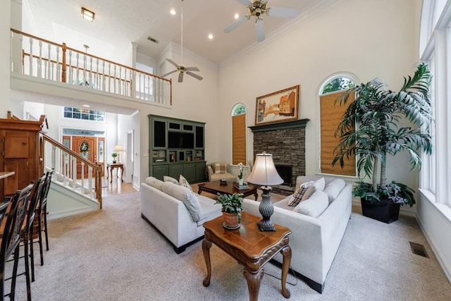 carpeted living room featuring a ceiling fan, a high ceiling, crown molding, a fireplace, and stairway