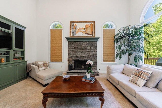 living room featuring light colored carpet, a high ceiling, healthy amount of natural light, and a stone fireplace