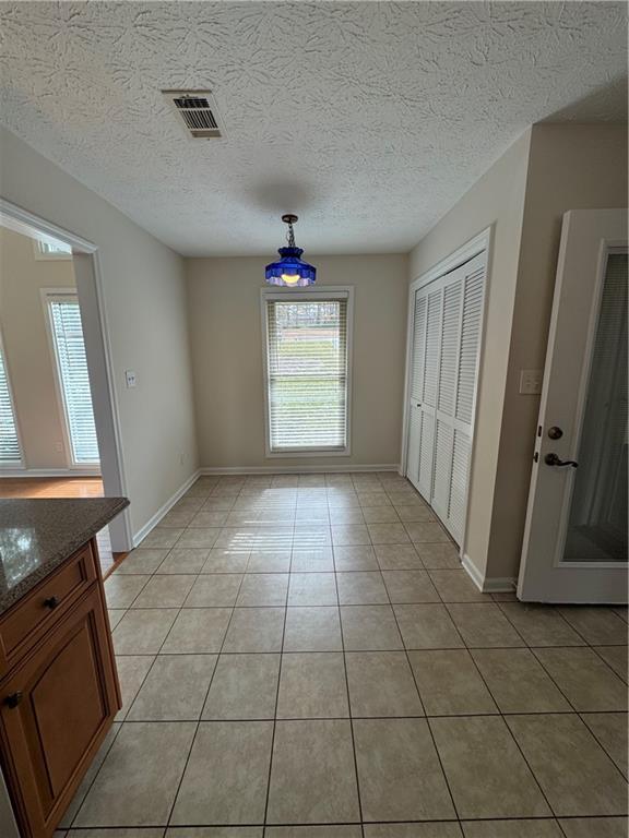 unfurnished dining area featuring light tile patterned flooring and a textured ceiling