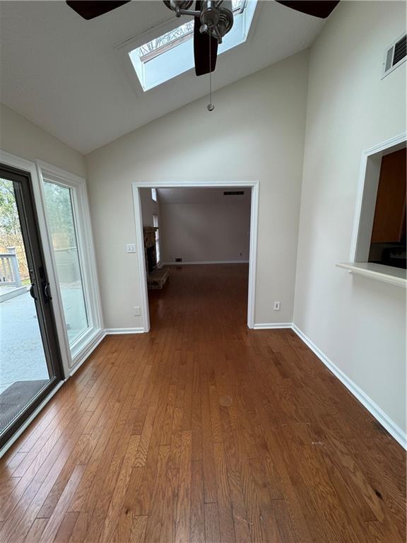 unfurnished room with hardwood / wood-style flooring, lofted ceiling with skylight, and ceiling fan