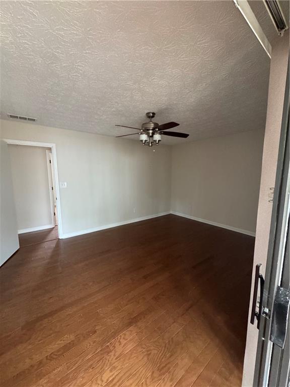 empty room with ceiling fan, wood-type flooring, and a textured ceiling