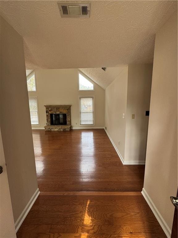 unfurnished living room featuring wood-type flooring, a stone fireplace, vaulted ceiling, and a healthy amount of sunlight