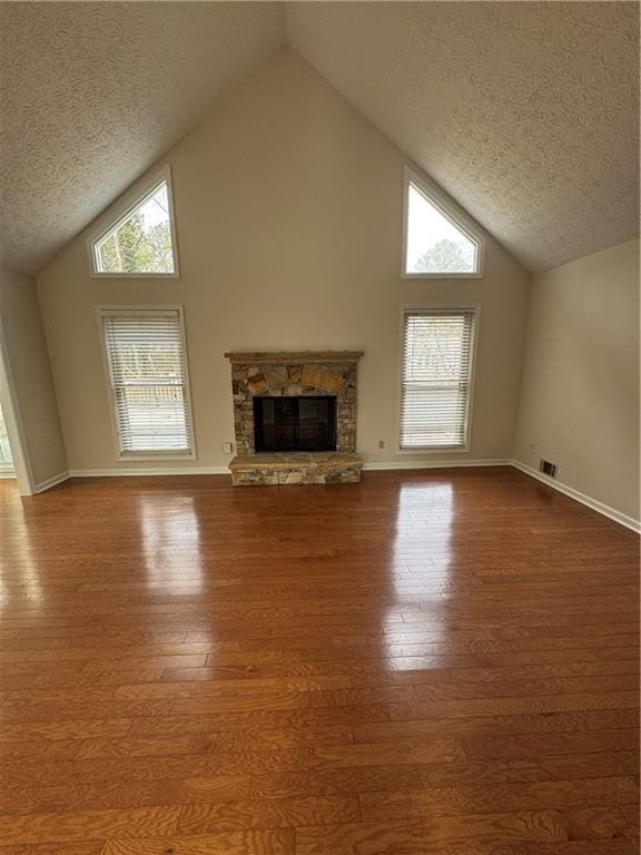 unfurnished living room with hardwood / wood-style flooring, a wealth of natural light, a textured ceiling, and a fireplace