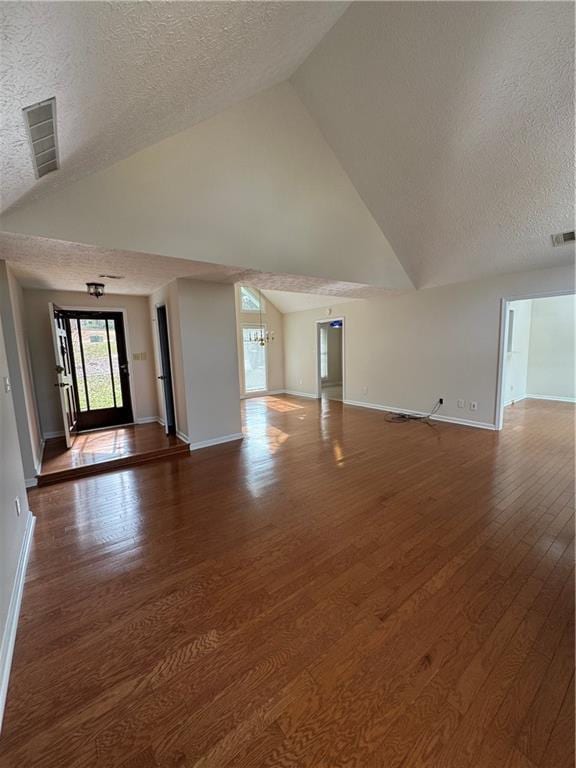 unfurnished living room with high vaulted ceiling, dark wood-type flooring, a textured ceiling, and a chandelier