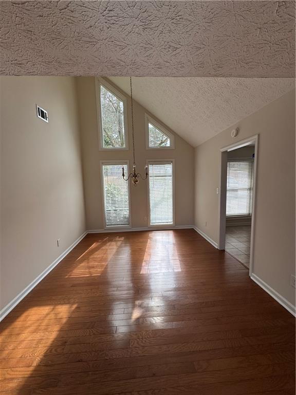 unfurnished room with vaulted ceiling, a chandelier, a textured ceiling, and dark hardwood / wood-style flooring