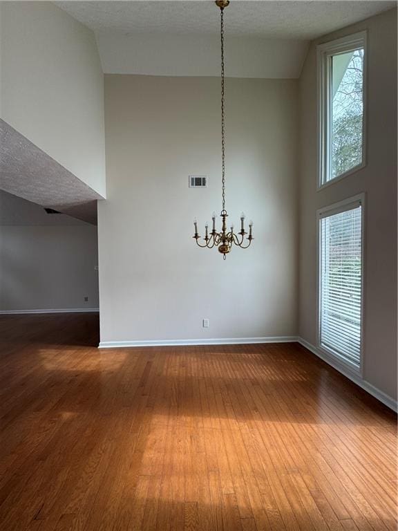 unfurnished dining area featuring hardwood / wood-style flooring, a notable chandelier, and high vaulted ceiling