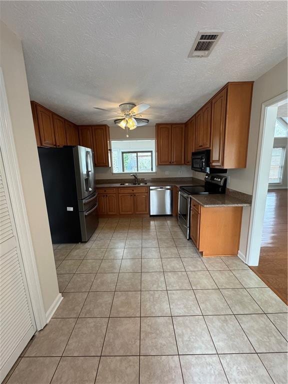 kitchen with sink, light tile patterned floors, ceiling fan, stainless steel appliances, and a textured ceiling