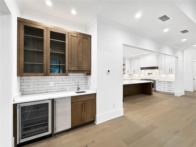 bar featuring white cabinets, sink, beverage cooler, stainless steel appliances, and light wood-type flooring