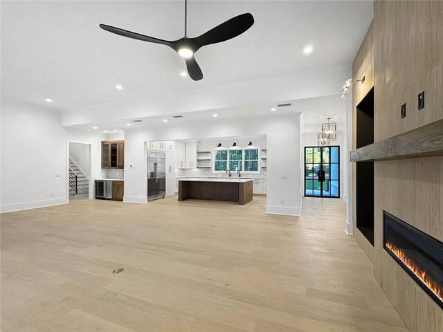 unfurnished living room with ceiling fan with notable chandelier, a tiled fireplace, and light hardwood / wood-style floors