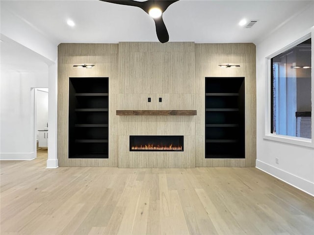 unfurnished living room featuring ceiling fan, a fireplace, built in features, and light hardwood / wood-style flooring