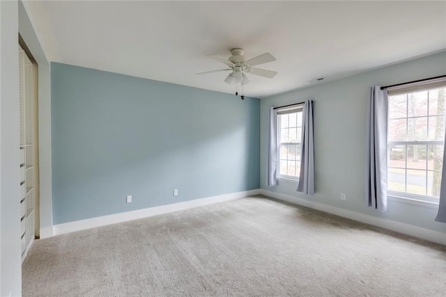 carpeted spare room with visible vents, baseboards, and a ceiling fan