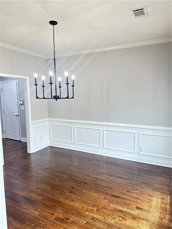 540 Langley Creek Dr, Loganville, GA 30052 - unfurnished dining area featuring crown molding, a chandelier, dark wood-style flooring, wainscoting, and a decorative wall