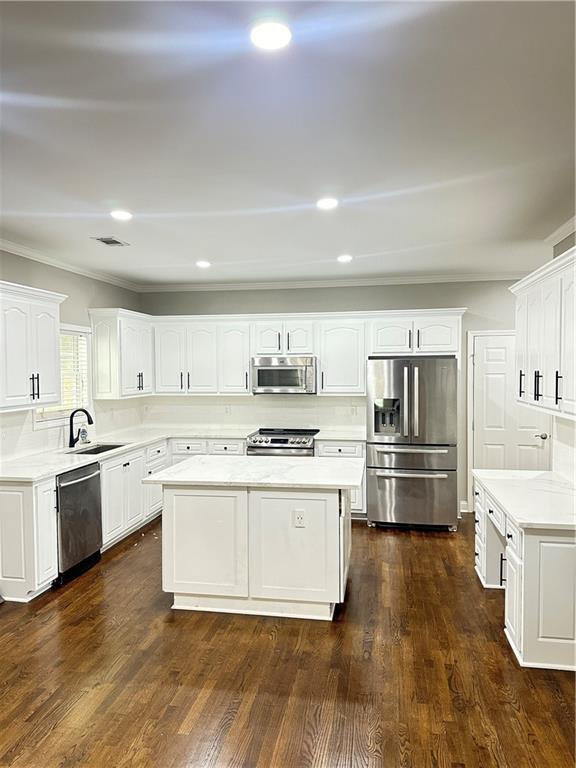 540 Langley Creek Dr, Loganville, GA 30052 - kitchen with appliances with stainless steel finishes, a center island, white cabinetry, light countertops, and dark wood-type flooring