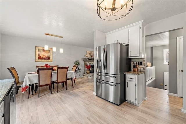 kitchen featuring light wood-style floors, a textured ceiling, stainless steel fridge with ice dispenser, and light stone countertops