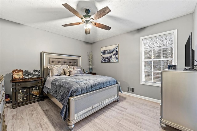 bedroom with a textured ceiling, ceiling fan, visible vents, baseboards, and light wood-type flooring