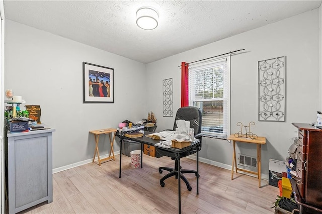 home office featuring light wood finished floors, baseboards, visible vents, and a textured ceiling