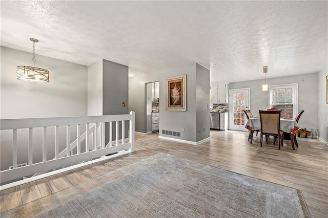 hallway featuring a textured ceiling, an upstairs landing, visible vents, baseboards, and light wood-type flooring