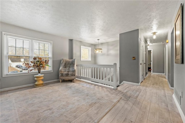 unfurnished room with light wood finished floors, baseboards, a textured ceiling, and an upstairs landing