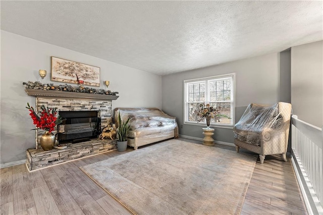 living area featuring a textured ceiling, a stone fireplace, and wood finished floors