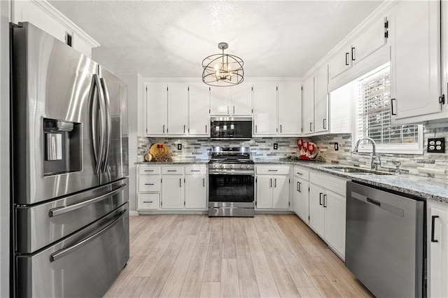 kitchen with light stone counters, appliances with stainless steel finishes, white cabinets, a sink, and light wood-type flooring