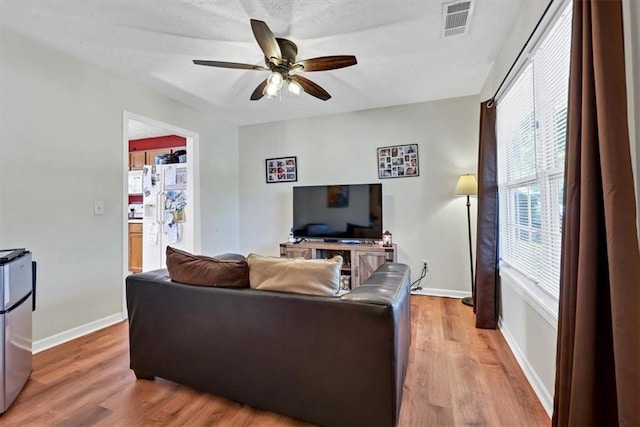 living room with light wood-type flooring, ceiling fan, and a textured ceiling