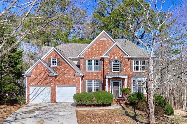 colonial-style house with an attached garage, roof with shingles, concrete driveway, and brick siding